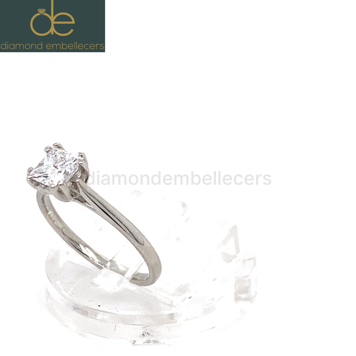 A princess-cut diamond solitaire ring in a platinum band, displayed on a clear acrylic stand against a white background. 