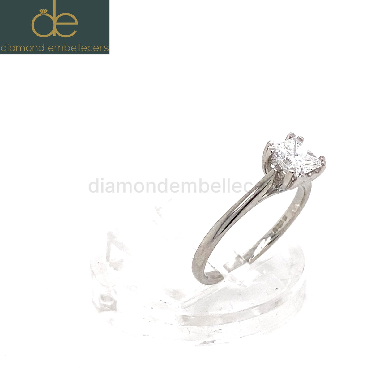 A princess-cut diamond solitaire ring in a platinum band, displayed on a clear acrylic stand against a white background. 