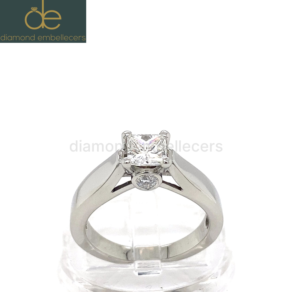 A white gold diamond engagement ring with a princess-cut center stone and a small round accent stone. 